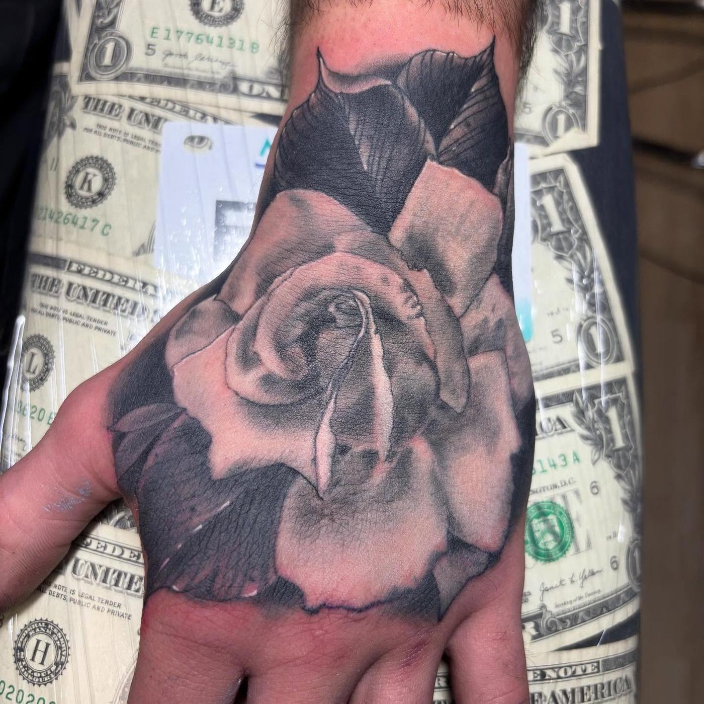 A black and gray rose tattooed across the back of a hand
