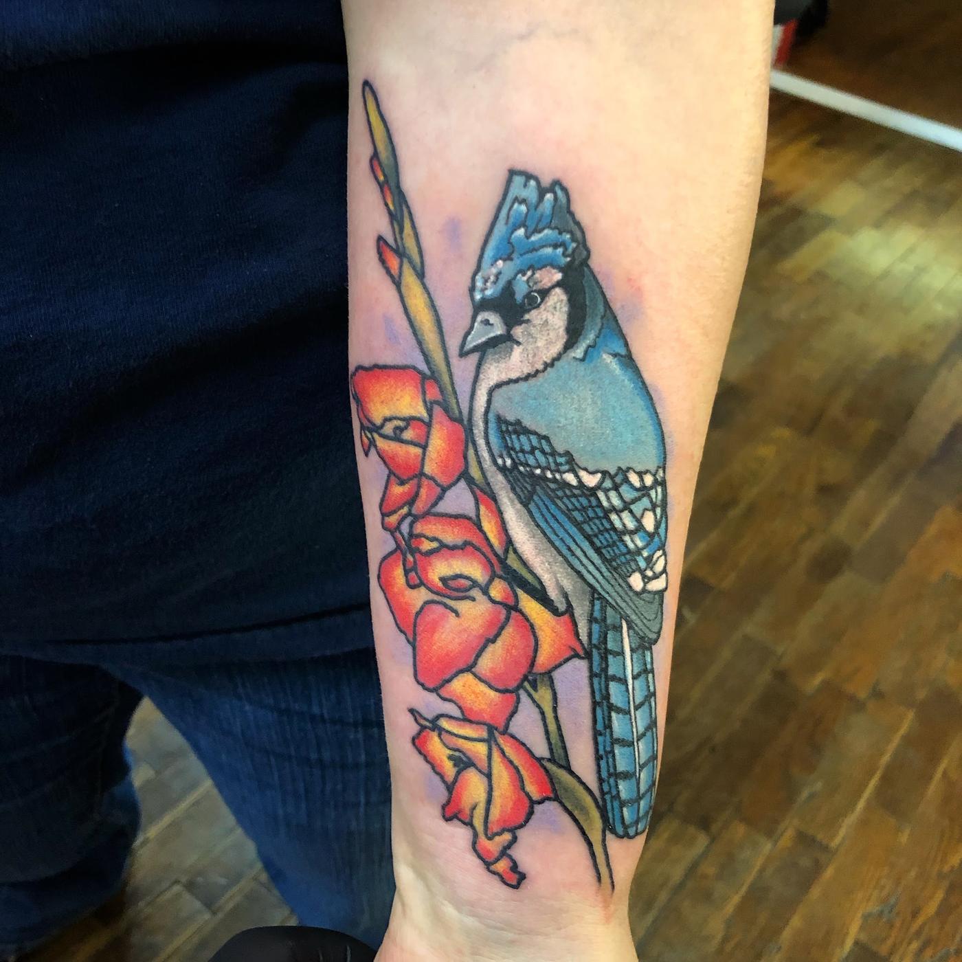 A color blue jay and poppies tattoo on a forearm